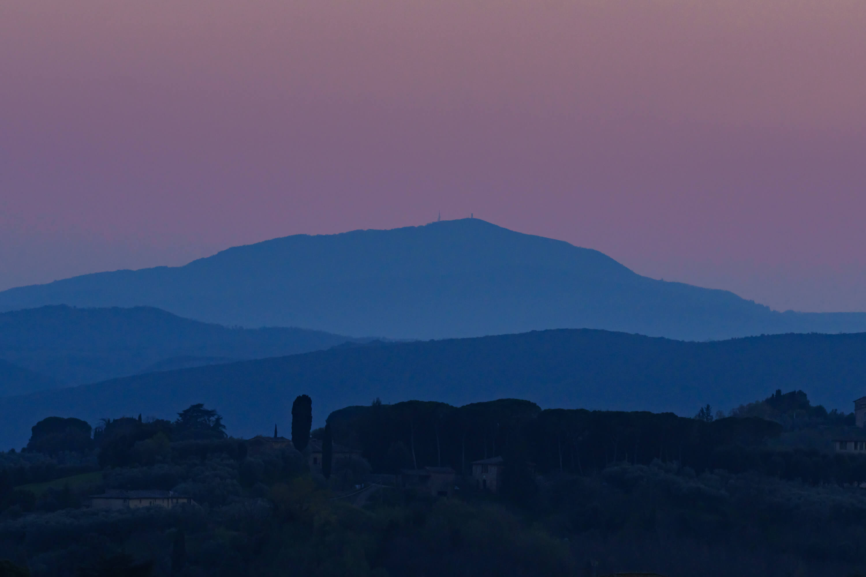 The hills that surround Siena are bathed in blue hour light. Four hills are covered by increasingly light hues of blue, purple, and haze.