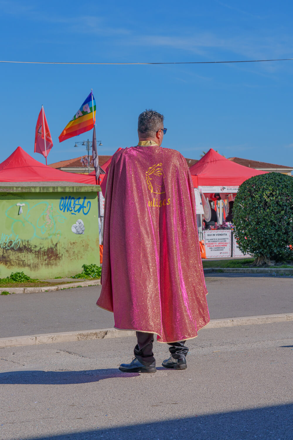 A man stands alone in Viareggio waiting for Carnevale to begin in full. He is adorned in a shiny pink and gold cape like a superhero.