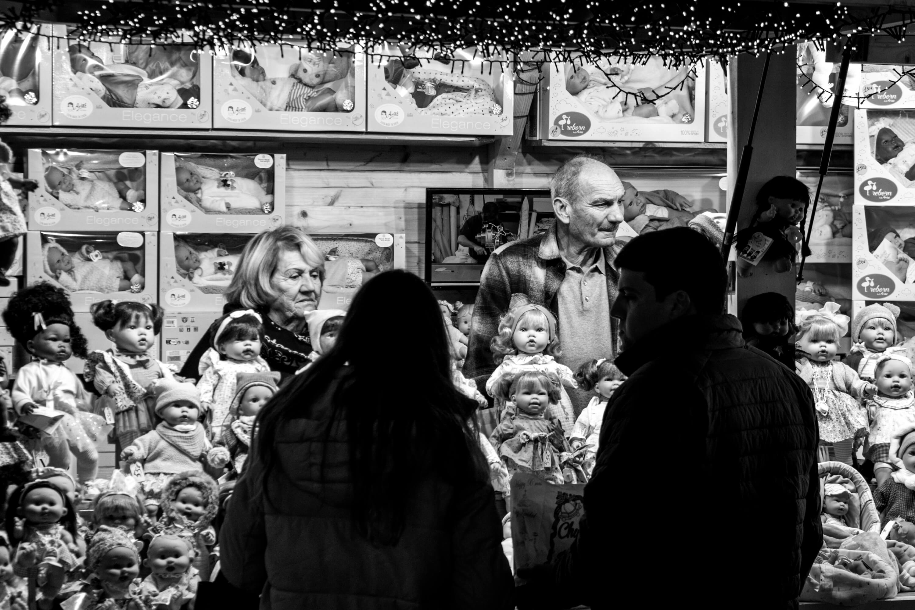 Opening weekend for the Christmas Market in Jardin des Tuileries. Two older vendors look on as people look at the dolls that fill their stall.