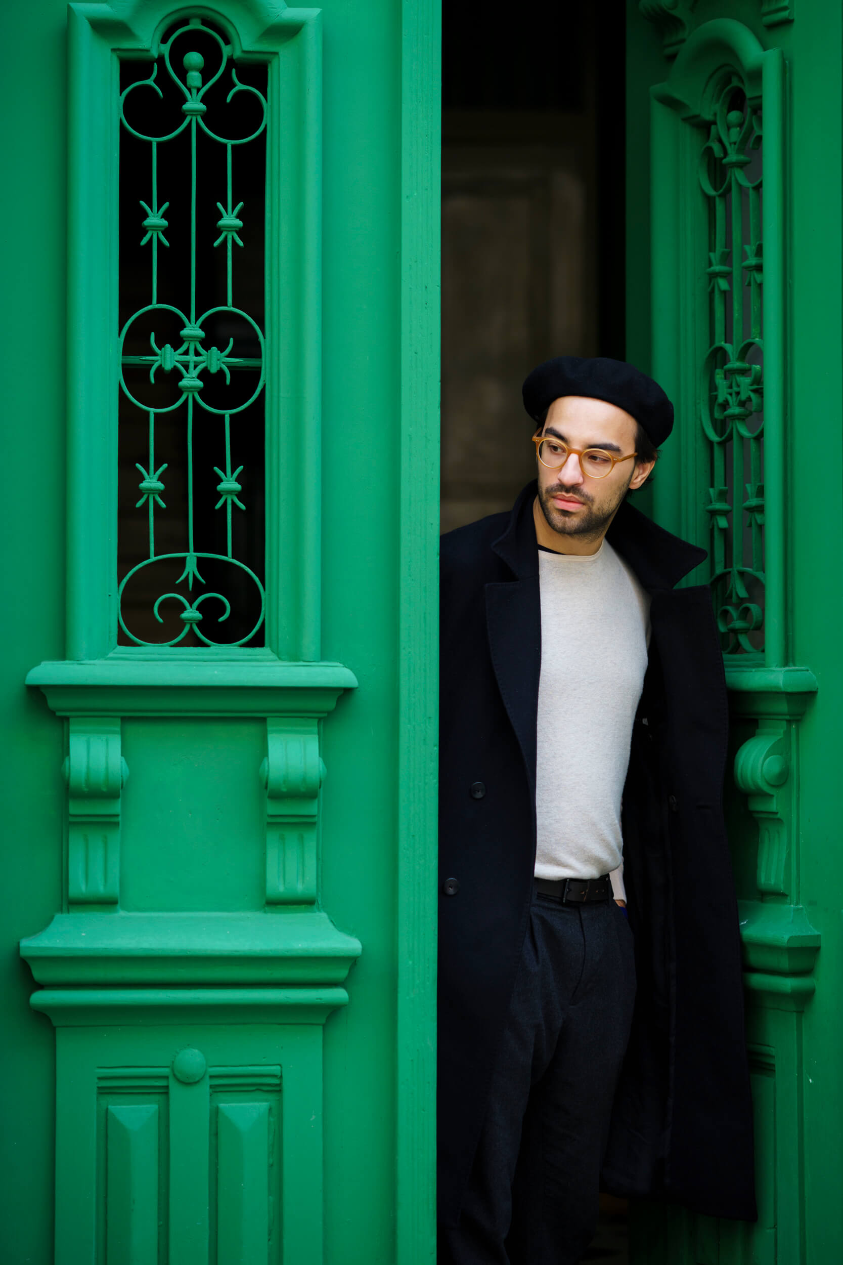 A model walks through a green door on a side street in Lisbon. He looks to be checking to make sure no one is coming.