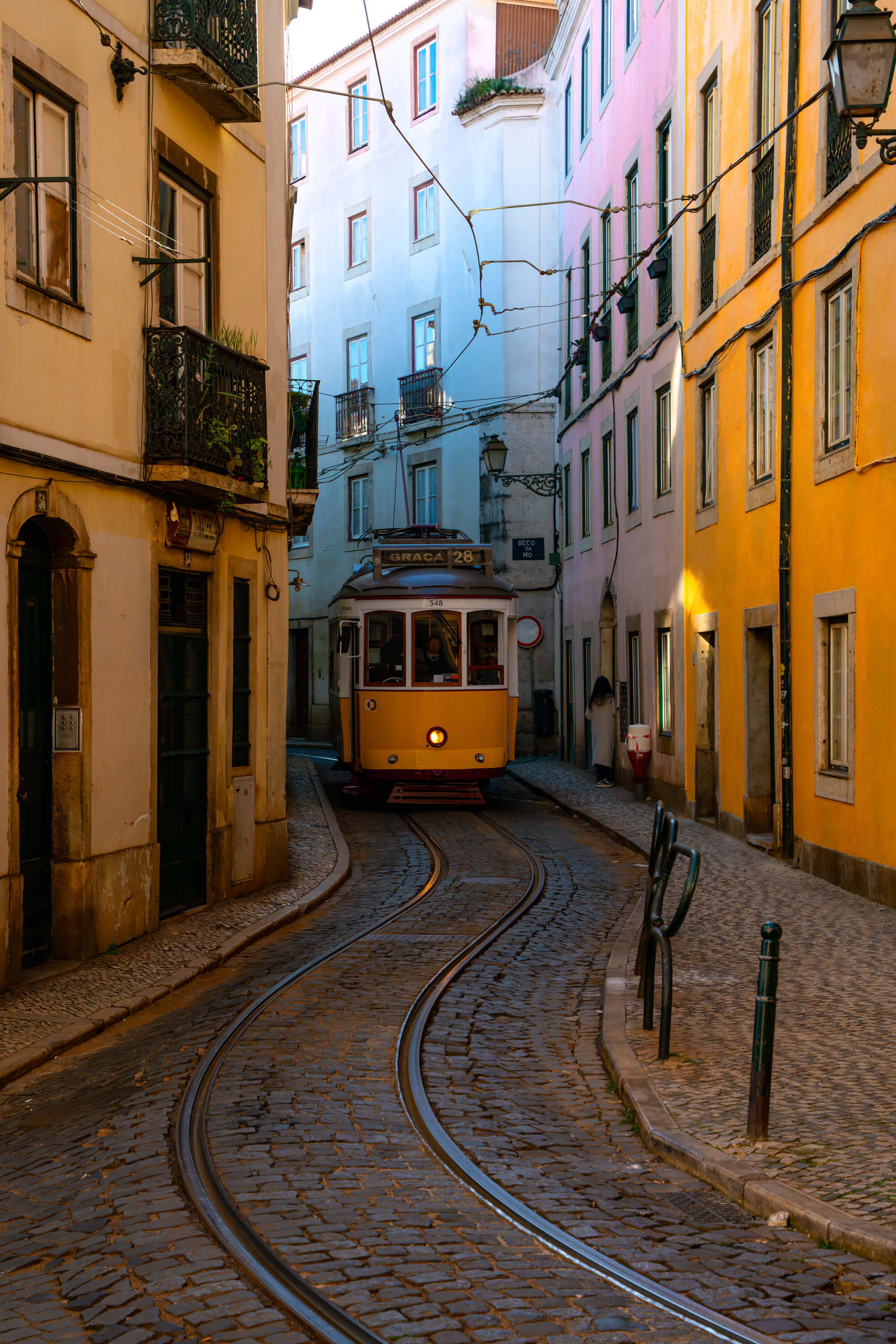 Lisbon's most famous yellow tram rounds the bends on its way to Graça, making its way through bright yellow, blue, and pink buildings.