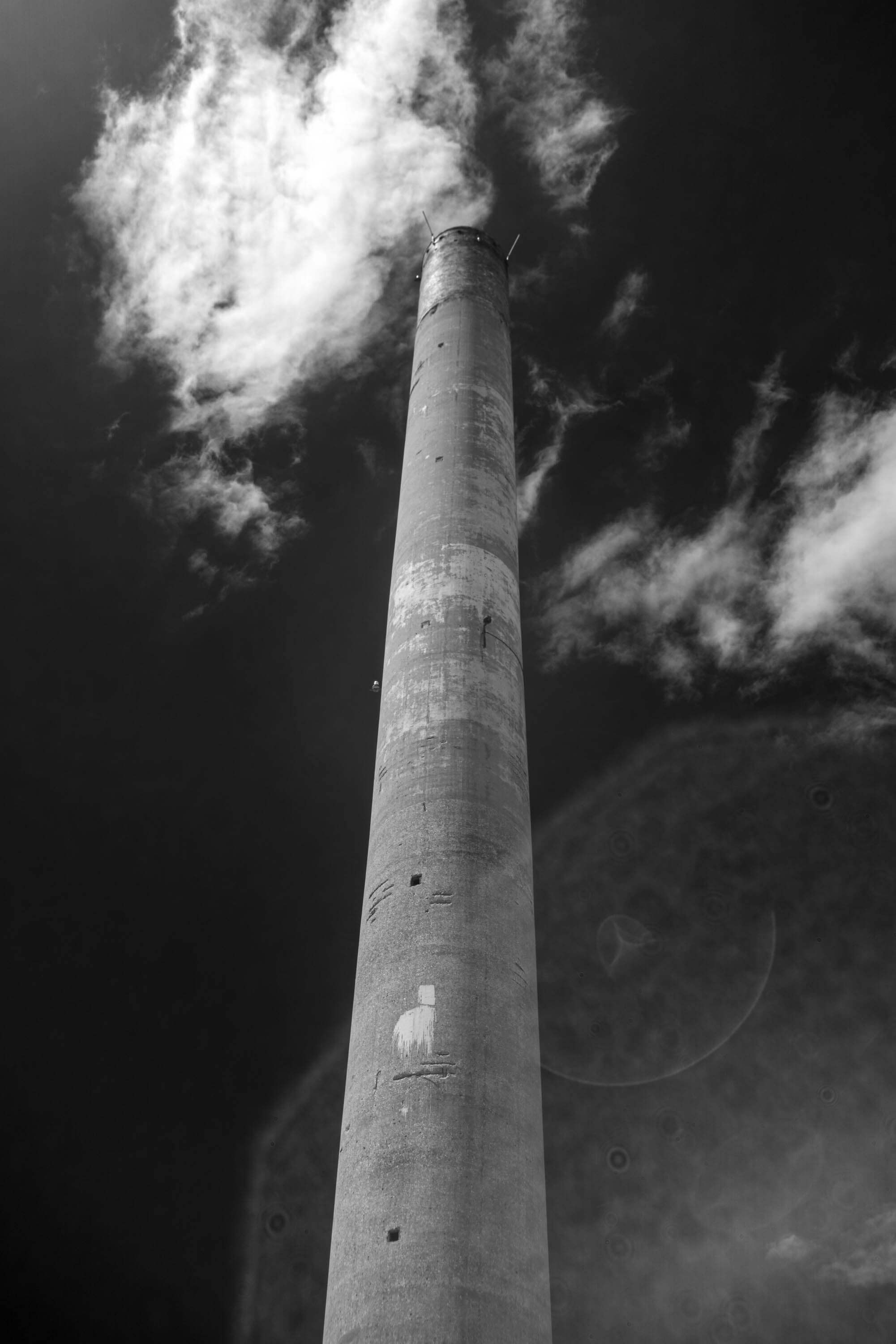A large smokestack stands alone in Barreiro, Portugal against a sky darkened by infrared. A light flare normally hidden is easily visible in the infrared light.