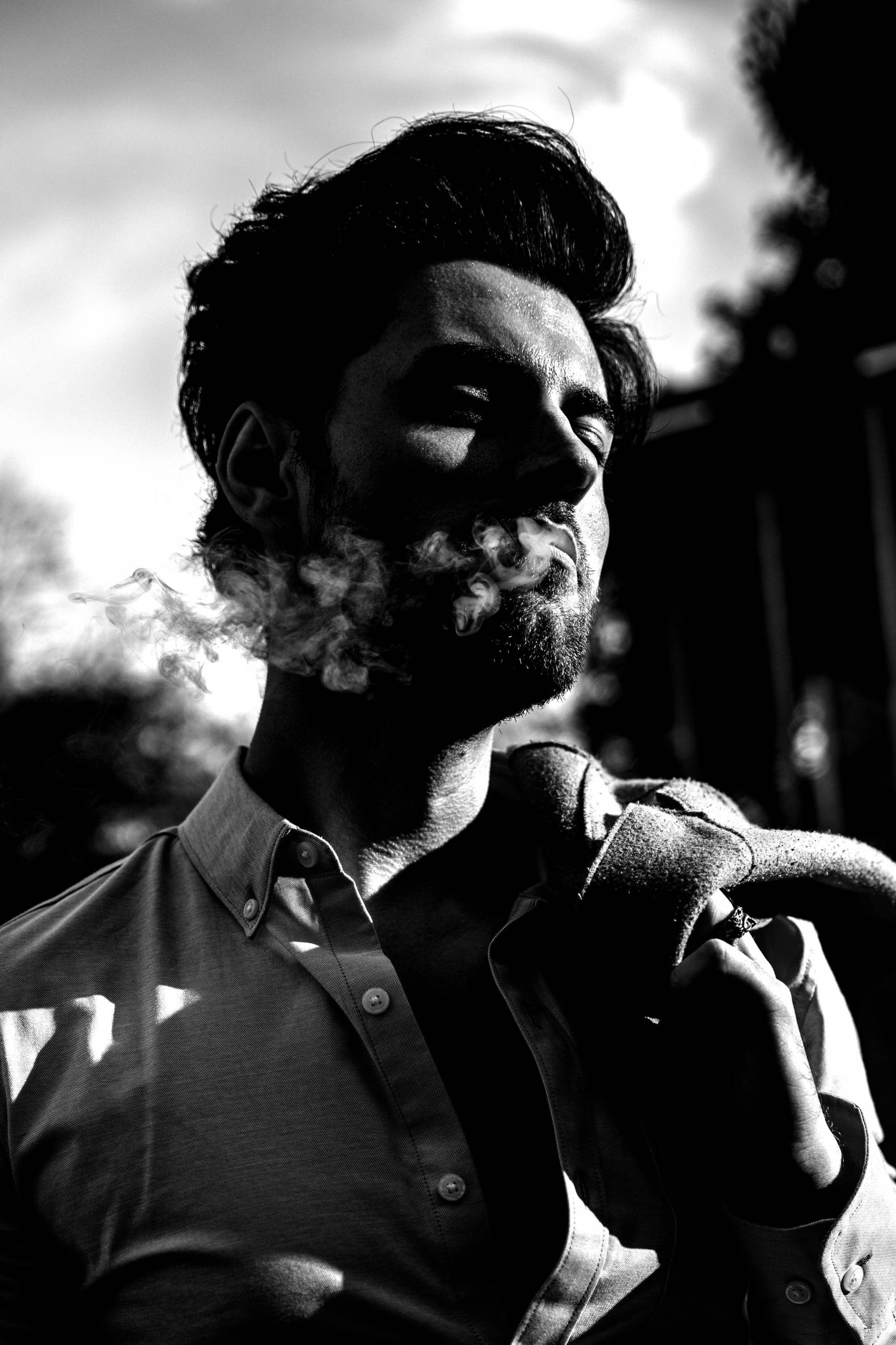 A model is smoking while bathed in shadow and light. The light and shadow gives definition to the smoke.